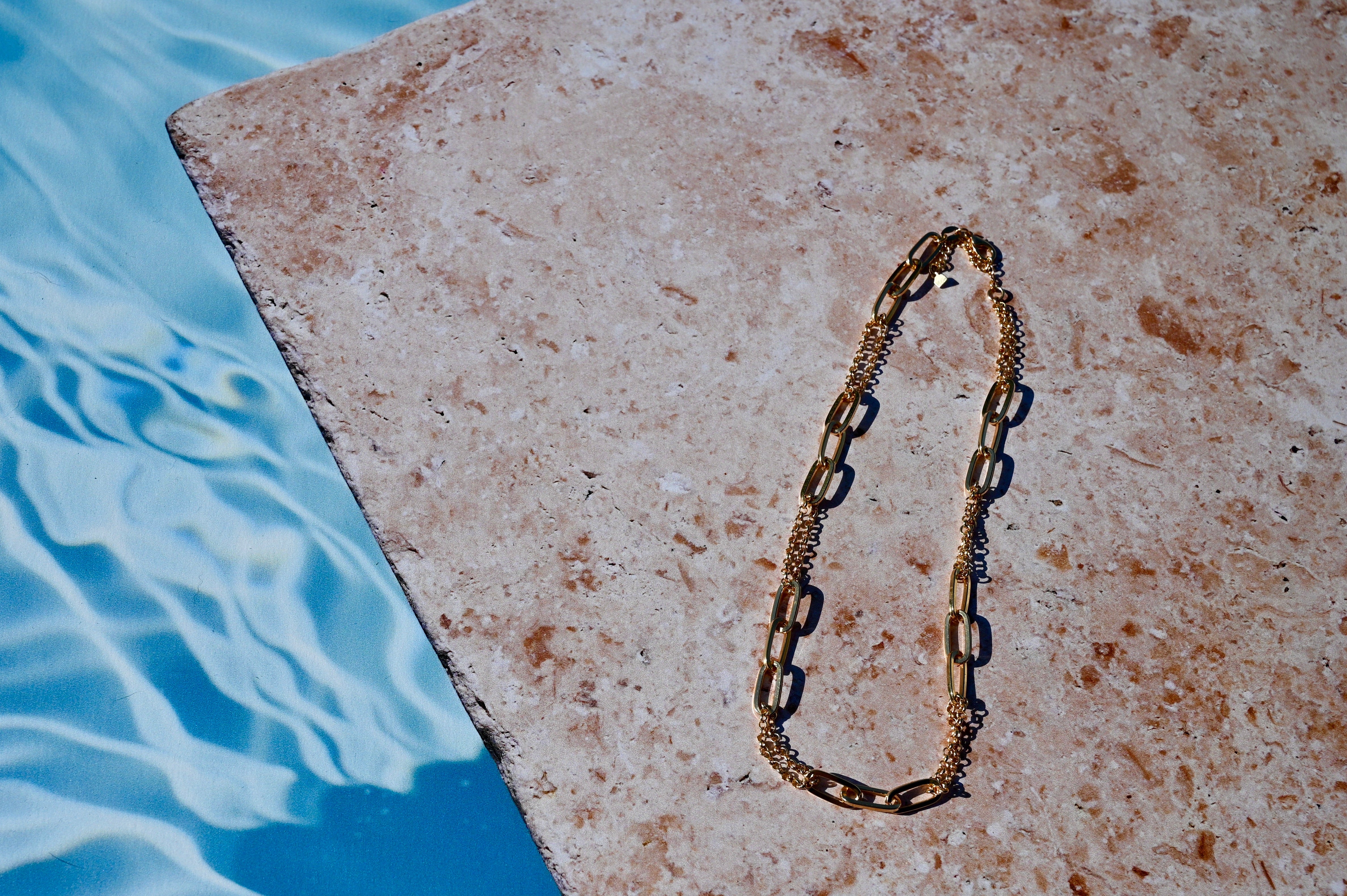 Gold chain necklace on a stone ledge by a pool